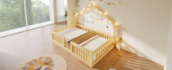 Houten kinderbed met hekjes en dak met kerstlichtjes, beddengoed met sterretjes, deken en rond vloerkleed.