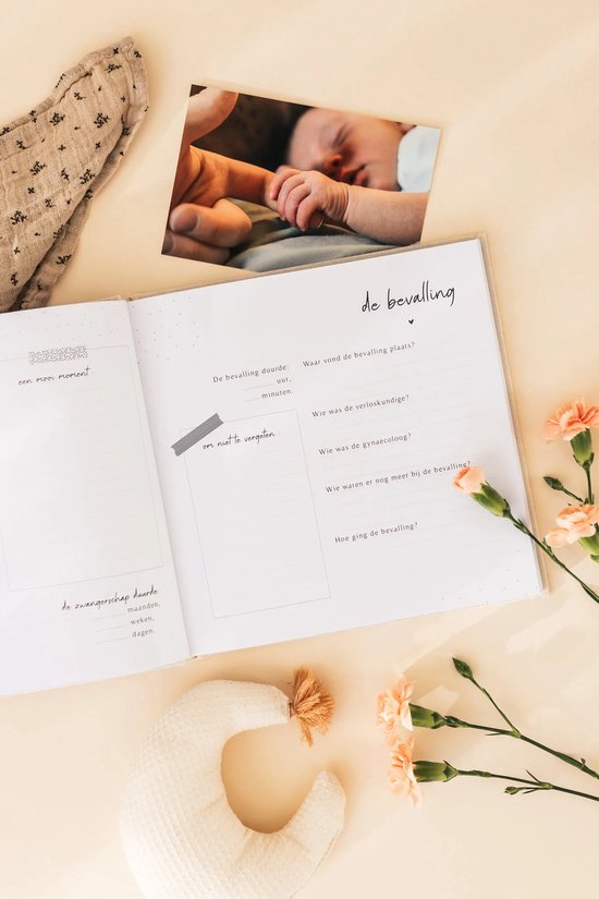 Babyboek open, met een foto van een babyhandje, tekst over de bevalling en een babymobiel.