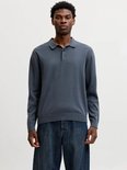 Man draagt een donkerblauwe gebreide poloshirt met lange mouwen en jeans.