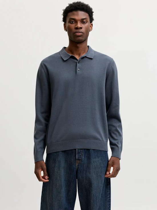 Man draagt een donkerblauwe gebreide poloshirt met lange mouwen en jeans.