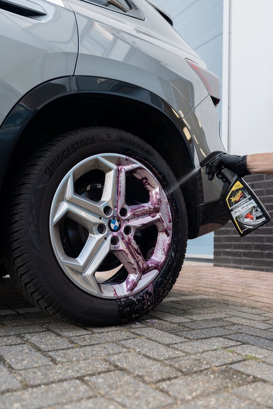 Hand met handschoen spuit velgenreiniger op een zilveren BMW velg. De reiniger kleurt rood.