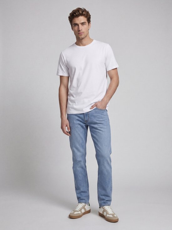Man met witte t-shirt en lichtblauwe, rechte jeans met bruin label en sneakers.