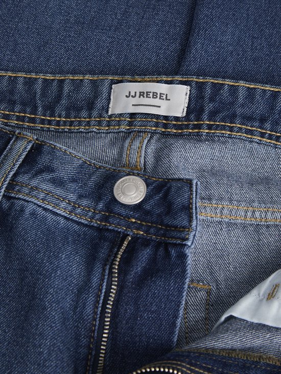 Sluiting en tailleband van een blauwe JJ REBEL spijkerbroek met JJ REBEL logo.