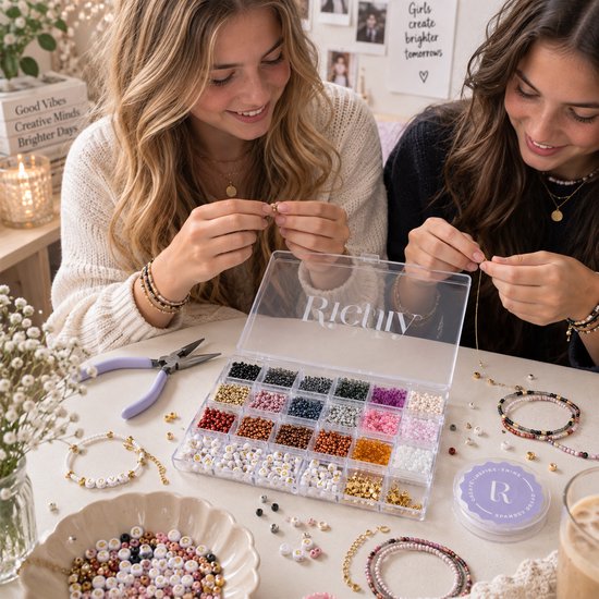 Twee meisjes maken sieraden met een kralendoos met gouden en herfstkleurige kralen, letterkralen, bedels en tang.