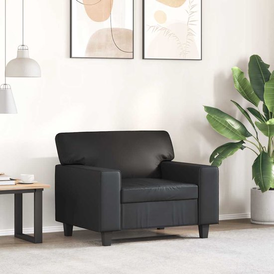 Zwarte fauteuil in een woonkamer met abstracte muurkunst en een grote plant.
