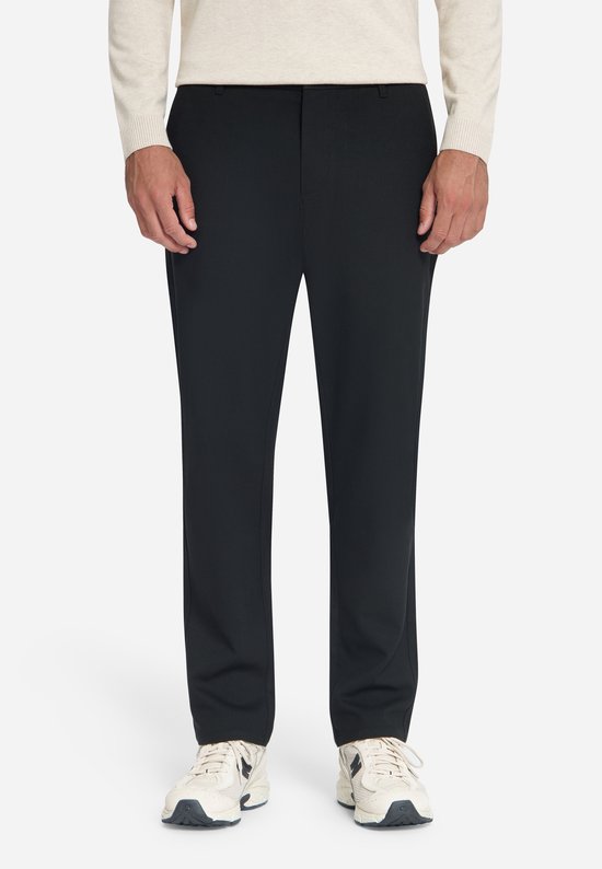 Zwarte chino-broek in een moderne pasvorm, gedragen met een beige trui en sneakers.
