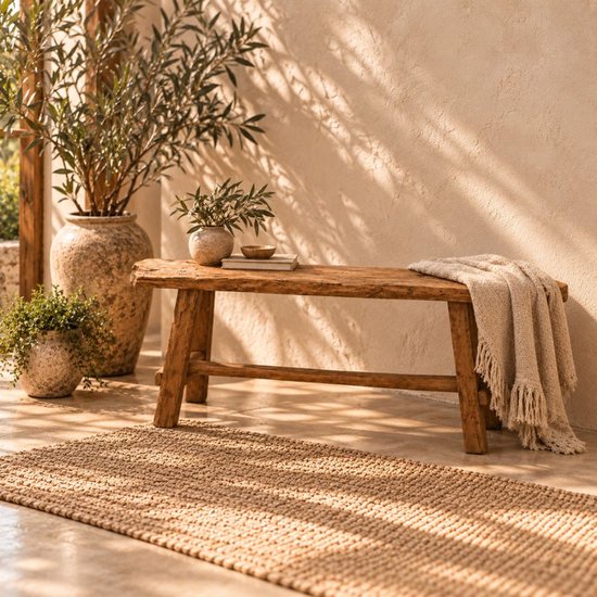 Een verweerde, houten bank met een gebreide plaid en planten in terracotta potten.