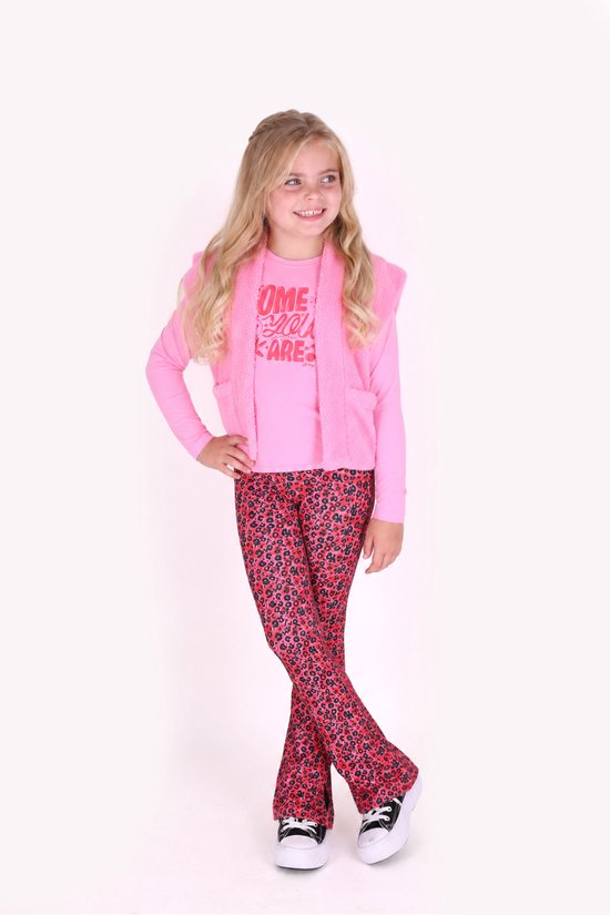 Meisje draagt een roze shirt met tekst, roze bodywarmer en rode flared broek met bloemenpatroon.
