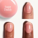 Een ronde roze dop met 'Sugar Daddy' in witte letters, naast close-ups van nagels met lichtroze nagellak.