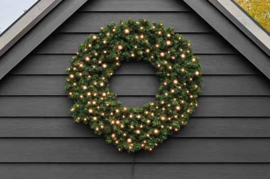 Grote, verlichte kunstkerstkrans met warmwitte LED-lampjes aan een donkergrijze muur.