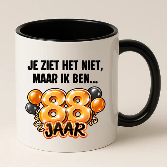 Witte mok met zwart handvat, tekst 'Je ziet het niet, maar ik ben... 88 jaar' en afbeelding van 88 met ballonnen.