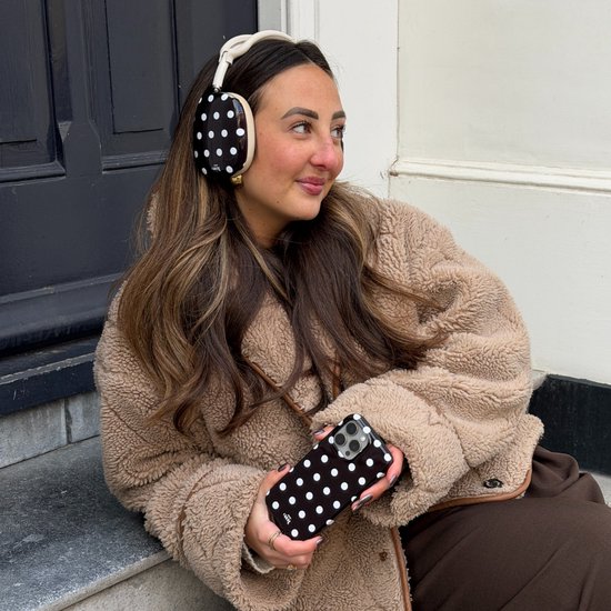 Jonge vrouw met koptelefoon en telefoonhoesje met zwart-wit stippatroon. Koptelefoon met stippen.