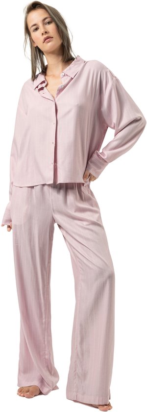 Model in roze pyjamaset met subtiele strepen, poseren met één hand op de heup en het overhemd deels open.