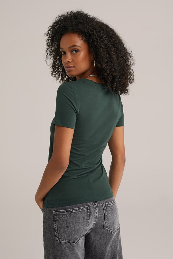 Model met donkergroen t-shirt met korte mouwen en grijze jeans, van achteren gezien.