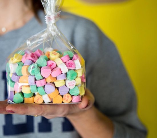 Een persoon houdt een zak gevuld met kleurrijke snoepjes in de vorm van hartjes vast.