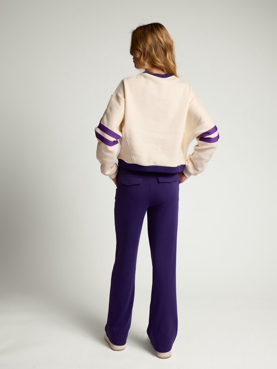 Achterkant van ecru sweater met paarse accenten op de mouwen, gecombineerd met een paarse broek.