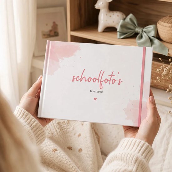Handen houden een wit invulboek voor schoolfoto's vast, versierd met roze aquarel en een roze elastiek.