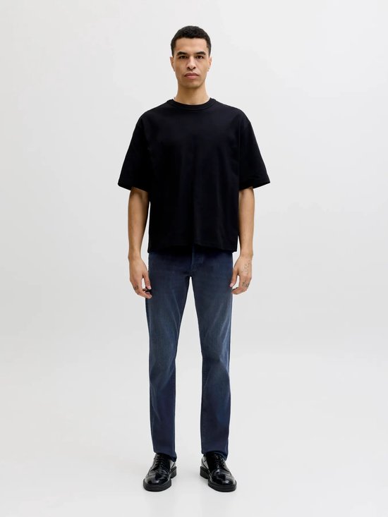 Man met een zwarte oversized t-shirt en blauwe jeans.