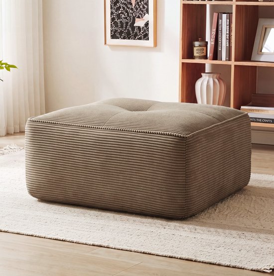 Een vierkante, bruine ribstof poef in een woonkamer, op een vloerkleed.