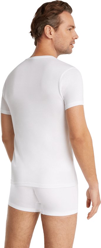 Man in wit V-hals T-shirt en witte boxershorts, staand met rug naar de camera.