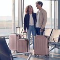 Een lachend stel met roze koffers in een luchthaven wachtruimte.
