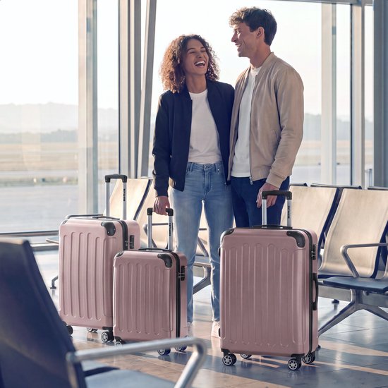 Een lachend stel met roze koffers in een luchthaven wachtruimte.