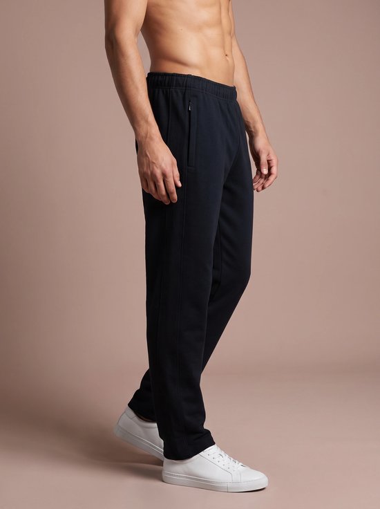 Man van opzij in donkerblauwe sportbroek met ritssluiting, witte sneakers.