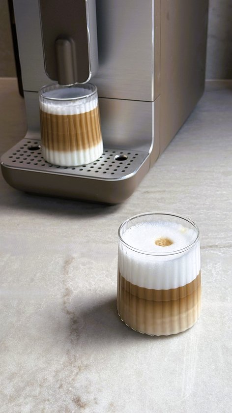 Deux verres côtelés, remplis de café stratifié avec de la mousse de lait, à côté d'une machine à café.