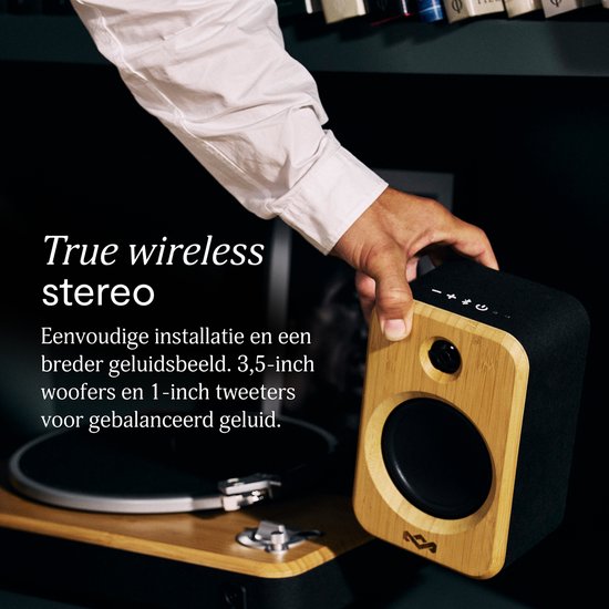 Hand houdt bamboe en zwarte draadloze luidspreker vast bij een platenspeler.