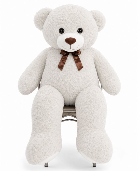 Grote witte teddybeer van zachte pluche met een bruine strik om de nek, zittend op een stoel.
