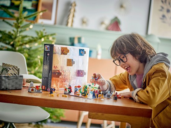 Jongen met bril speelt met LEGO Marvel Avengers adventskalender, met minifiguren en kerstdecoraties.