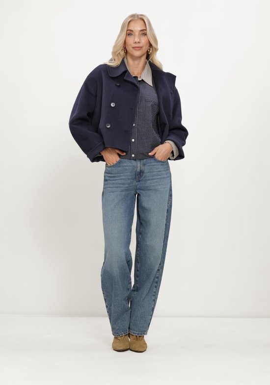 Een model draagt een blauwe spijkerbroek met wijde pijpen, een geruit overhemd en een donkerblauwe jas.