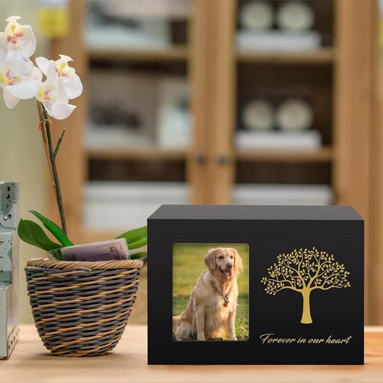 Zwarte houten dierenurn met goudkleurige levensboom op een tafel naast een witte orchidee in een gevlochten mand.