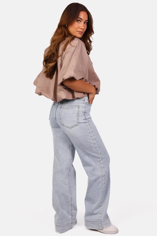 Achteraanzicht van een model in een taupe ballon-top en lichtblauwe jeans met studs langs de zijkanten.