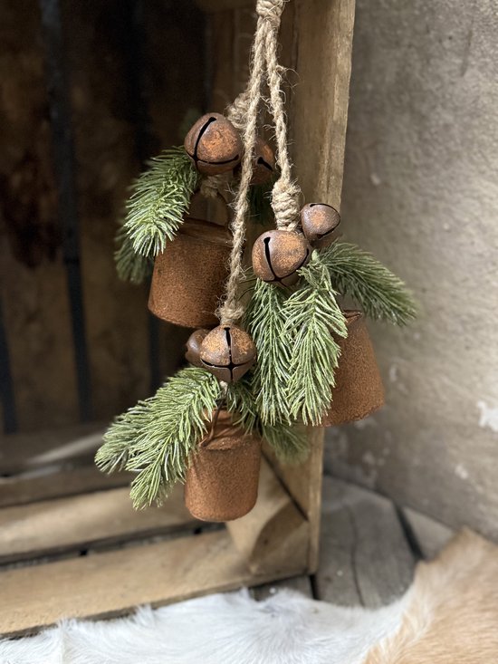 Landelijk kerstornament: roestkleurige koebellen met kunstmatige dennentakken aan een touw.
