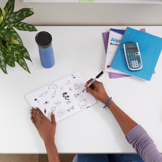 Vrouw tekent diverse figuurtjes met een zwarte Sharpie marker in een schetsboek.