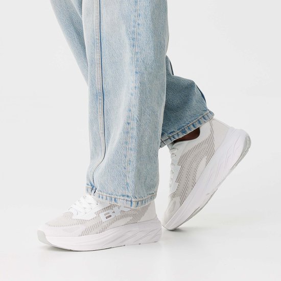Witte lage sneakers met een gebroken wit patroon en lichtblauwe jeans.
