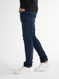 Man in donkerblauwe slim fit jeans met witte sneakers, van opzij gezien.