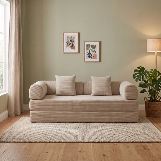 Lichtbeige ribstof slaapbank met twee bijpassende kussens en afgeronde armleuningen, staand op een beige vloerkleed.