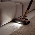 Gouden stofzuigmond met LED-verlichting onder een bank, zuigt vuil van laminaat en tapijt.