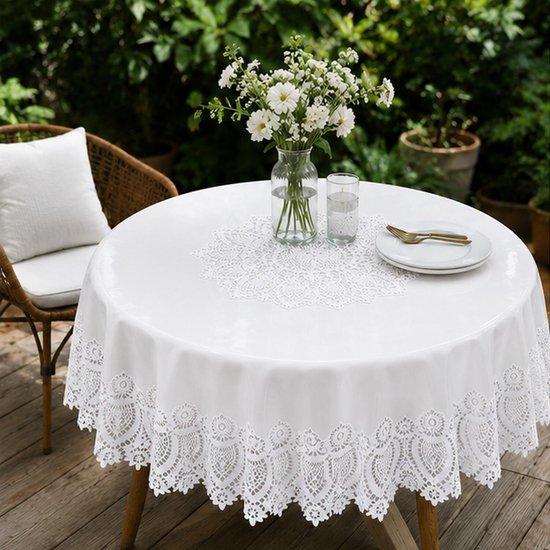 Ronde witte tafel met een kanten tafelkleed en onderlegger, buiten op een houten terras.