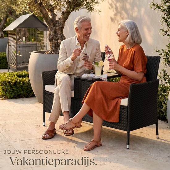 Een ouder koppel geniet van ijs op een zwarte polyrattan tuinbank met tafel in een zonnige tuin.