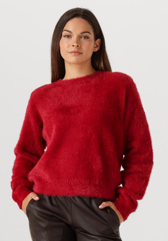 Een model met lange bruine haren draagt een rode, pluizige trui met lange mouwen.