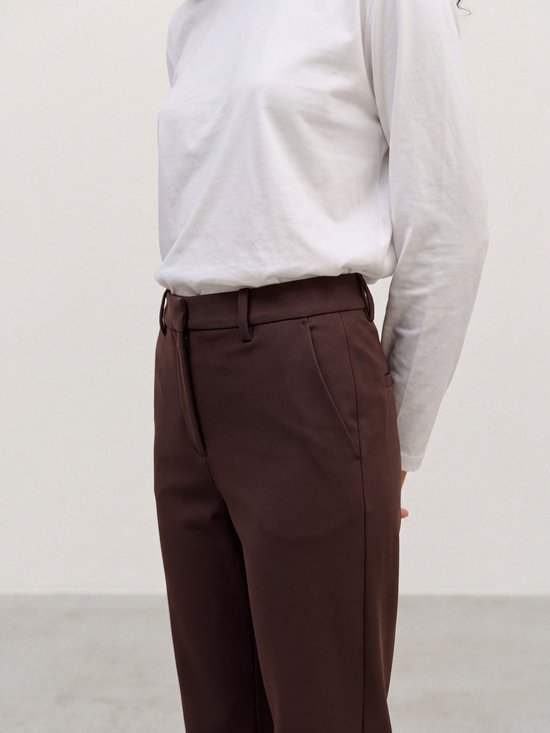 Close-up van een donkerbruine pantalon gecombineerd met een eenvoudig wit shirt met lange mouwen.