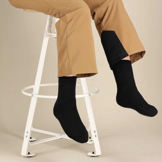 Persoon draagt zwarte thermische kindersokken op een witte kruk, zittend in beige broek.