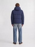 Man met de rug naar voren, draagt een blauwe pufferjas met capuchon en wijde jeans.