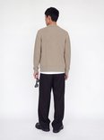 Achteraanzicht van model in beige gebreide polo met zwarte broek.