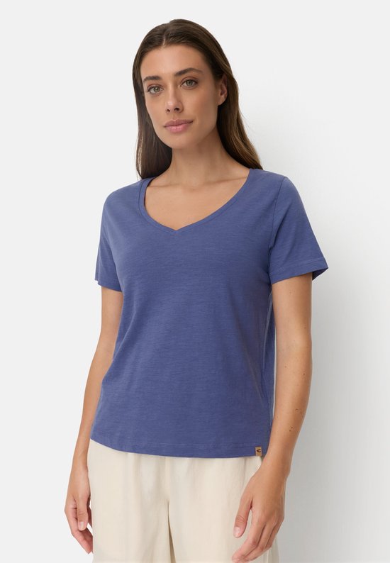 Close-up van een vrouw met lang bruin haar, draagt een blauw V-hals T-shirt.