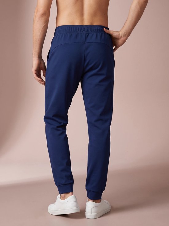 Achterkant van een marineblauwe joggingbroek met trekkoord en witte sneakers, gedragen door een man.