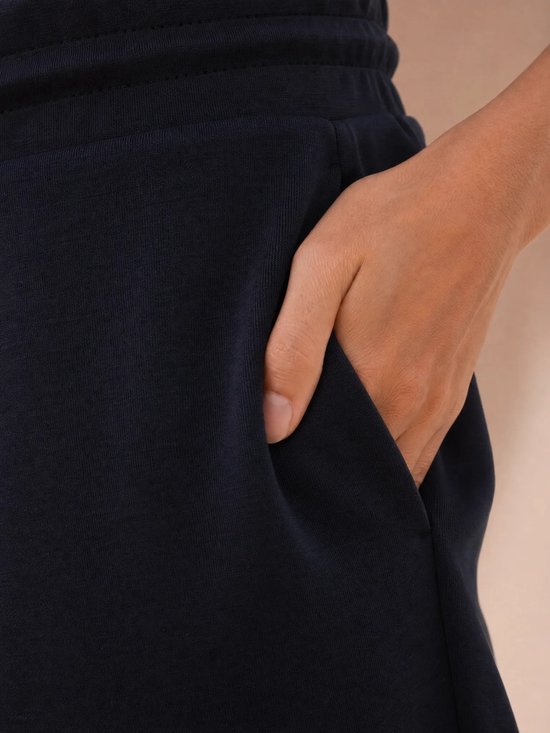 Close-up van de zak van een donkerblauwe sportbroek, met een hand erin gestoken.